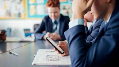 Getty Images/SolStock Young male student, wearing a blue uniform, using a mobile phone during a class (stock image)