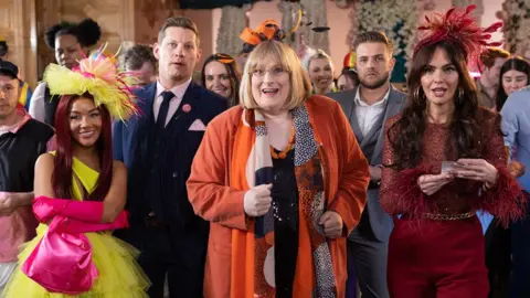 Lime Pictures/Channel 4 Assembled Hollyoaks characters dressed in colourful outfits at a wedding