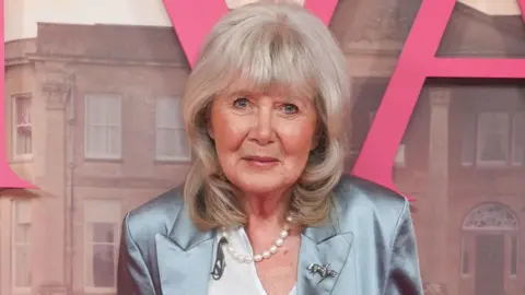 PA Dame Jilly Cooper at the premiere of Rivals standing against a poster for the Disney+ series.