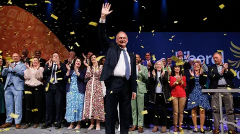  EPA Liberal Democrat leader Sir Ed Davey waves after delivering his keynote speech at Liberal Democrat Party Conference in Brighton, with confetti and rows of MPs clapping behind him.