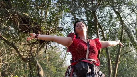 Siân Powell / @cornish_sian   Siân Powell in a red top in a forest