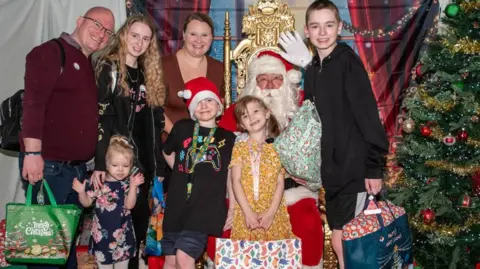 Family photo Lilly and Rachel with the Hamer family posing with Father Christmas and presents at the event. Lilly's three other siblings and father are also pictured. 