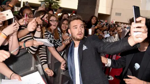 Getty Images Liam Payne taking a selfie with a large group of fans outside an award ceremony in 2015