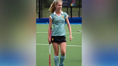 Clarissa's Campaign Clarissa Nicholls playing hockey at university. Miss Nicholls is wearing a light blue, short-sleeved, shirt bearing with the word "genei",  and long light blue socks. She is walking and carrying a pink, white and red hockey stick in her right hand.