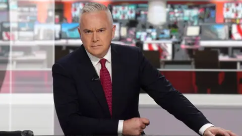 BBC Huw Edwards sitting behind the news desk on the BBC Ten O'clock News in 2022