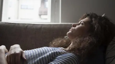 Getty Images A young woman lying down on a sofa, looking into the distance