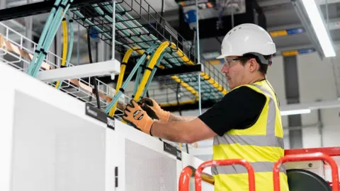 Datalec An engineer standing on a raised platform works on wiring in a datacentre.