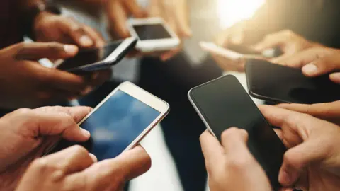 Getty Images Six smartphones are held by people facing in to a circle, we can only see their hands and those at the back of the shot are slightly out of focus.